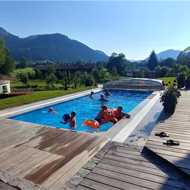 A beautiful pool in a sunny landscape. People are enjoying the water and the view of the mountains.