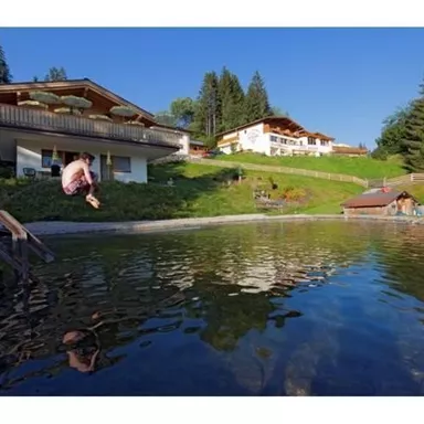 Ein ruhiger Teich umgeben von Bäumen und einer schönen Landschaft. Im Hintergrund sind mehrere Gebäude zu sehen, ideal für einen entspannenden Aufenthalt.