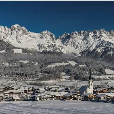 Eine malerische Winterlandschaft mit schneebedeckten Bergen und einem kleinen Dorf. Die Szene zeigt eine klare, blaue Himmel mit strahlendem Sonnenschein.