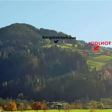 Ein schöner Berg mit grünem Gras und bunten Baumkronen. Markierungen zeigen die Standorte von Bergdokt Haus, MÖDLHOF und Gondelbahn Söll.