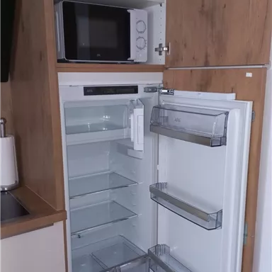 Ein moderner Kühlschrank mit transparenten Fächern und einer sauberen, aufgeräumten Innenansicht. Oben befindet sich eine Mikrowelle und einige Küchengeräte.
