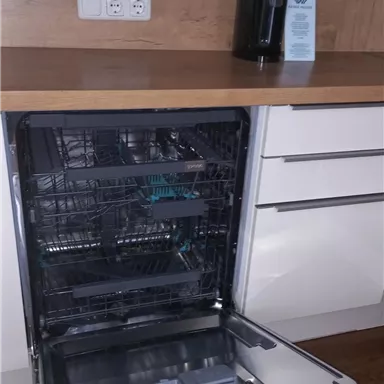 Eine moderne Küche mit einem offenen Geschirrspüler und einer Holzarbeitsplatte. Auf der Theke steht ein Wasserspender.