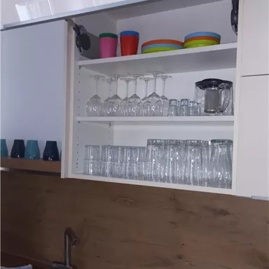 Eine moderne Küche mit einem offenen Küchenregal. Darin stehen Gläser, Becher und eine Karaffe auf einem Holzregal.