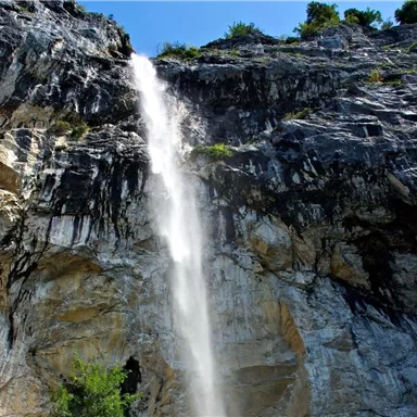 Ein beeindruckender Wasserfall, der von einer hohen Felswand herabstürzt. Die Umgebung besteht aus natürlichen Klippen und üppigem Grün.