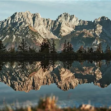 Eine beeindruckende Berglandschaft mit schroffen Gipfeln und einem klaren See im Vordergrund. Die Berge spiegeln sich ruhig im Wasser.