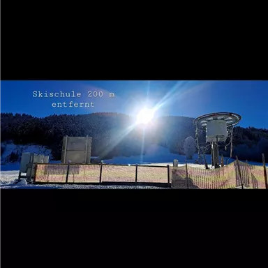 A ski school in winter with a large ski lift and snow. The sun shines brightly over the mountain landscape.