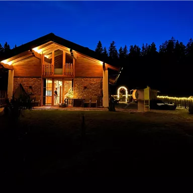 Ein wunderschönes Holzhaus mit warmem Licht im Dunkeln. Der Garten ist gemütlich und von Bäumen umgeben.