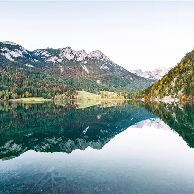 A tranquil lake, surrounded by mountains and forests. The landscape is clearly reflected in the water.