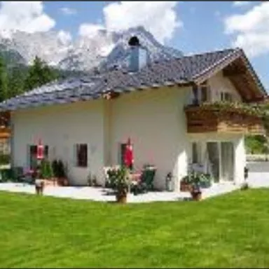 A modern house with a well-maintained garden and terraces. In the background, mountains can be seen under a clear sky.