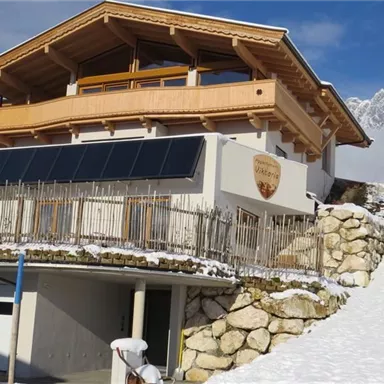 Ein modernes Haus mit Holzelementen in einer schneebedeckten Landschaft. Im Hintergrund sind die Berge sichtbar und der Himmel ist klar.