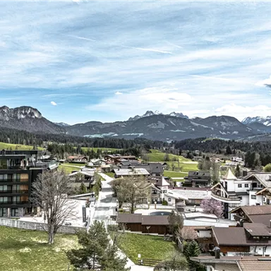Eine malerische Landschaft mit einem kleinen Dorf inmitten von Bergen. Der Himmel ist klar und die Umgebung ist grün und einladend.