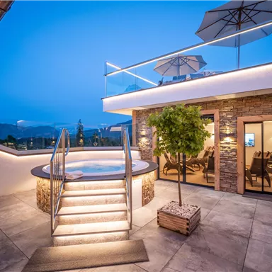 A modern terrace with a hot tub and cozy seating. The sky is blue and evening is approaching, creating a relaxed atmosphere.