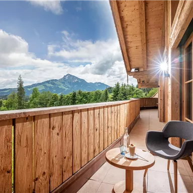 Ein Balkon mit Holzgeländer und schöner Aussicht auf die Berge. Ein Tisch und ein Stuhl laden zum Entspannen ein.