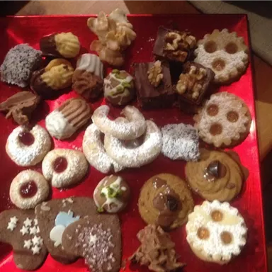 Ein buntes Arrangement von verschiedenen Plätzchen auf einem roten Teller. Die Leckereien sind in unterschiedlichen Formen und mit verschiedenen Toppings verziert.