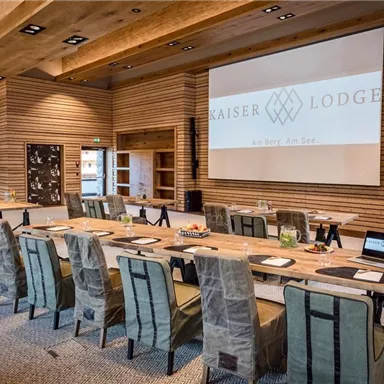 A modern conference room with a large table and several chairs. On the wall is a screen displaying the logo of the Kaiser Lodge.