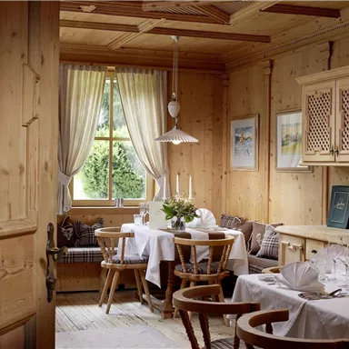 A cozy dining room with wood paneling and an inviting table. Large windows provide plenty of daylight and a friendly atmosphere.