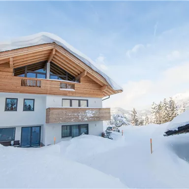 Ein modernes Haus im Schnee mit einem großen Holzdach. Die Umgebung ist winterlich und friedlich.