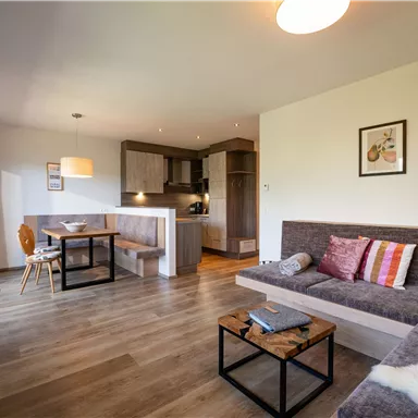 Ein modernes Wohnzimmer mit gemütlicher Couch und Esstisch. Die Küche ist offen und gut ausgestattet, mit warmem Licht und ansprechender Dekoration.