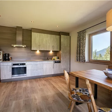 Moderne Küche mit Holzoberflächen und einer großen Fensterfront. Ein Esstisch aus Holz ergänzt den Raum und bietet eine gemütliche Atmosphäre.