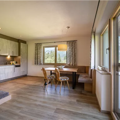 Eine moderne Küche mit Holzoberflächen und einem gemütlichen Essbereich. Große Fenster bieten einen Blick auf die Berge.