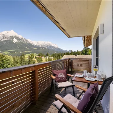 Ein schöner Balkon mit Blick auf die Berge. Auf dem Tisch stehen Frühstücksbere items und die Sonne scheint.