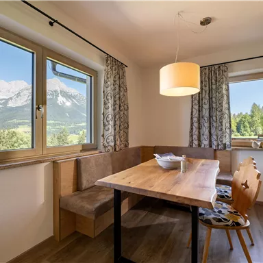 Ein heller Essbereich mit einem Holzstuhl und einem großen Tisch. Durch die Fenster hat man einen schönen Blick auf die Berge und die Natur.
