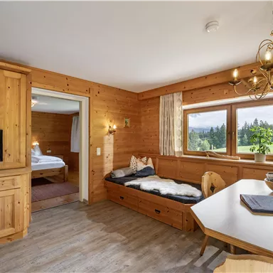 Ein gemütlicher Wohnbereich aus Holz mit einem Tisch und einem Sofa. Großen Fenstern bieten einen Blick auf die grüne Landschaft draußen.