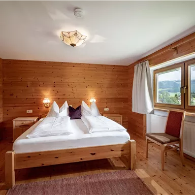 Ein gemütliches Schlafzimmer mit Holzverkleidung. Zwei Betten sind ordentlich angeordnet, und ein Fenster bietet einen Blick auf die Natur.
