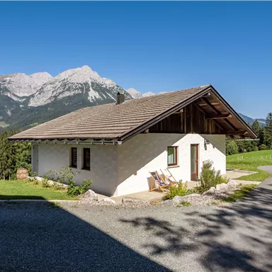 Ein gemütliches Haus in den Bergen mit einem klaren Himmel. Umgeben von grünen Wiesen und majestätischen Bergen.
