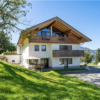 Ein modernes Haus mit einem schönen Holzdach und großen Fenstern. Es steht in einer grünen Umgebung mit Blick auf die Berge.