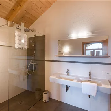 Ein modernes Badezimmer mit einer begehbaren Dusche und zwei Waschbecken. Die Holzdecke verleiht dem Raum eine warme Atmosphäre.
