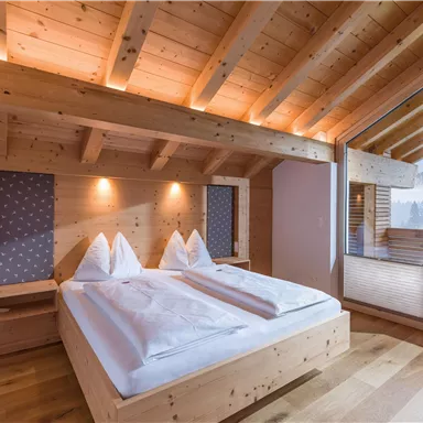 Ein gemütliches Schlafzimmer mit Holzwänden und einem großen Fenster. Es gibt zwei Betten mit weißen Bettdecken und eine einladende Atmosphäre.