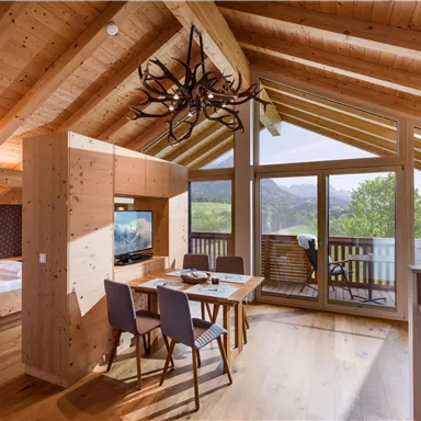 Ein gemütliches Zimmer mit Holzdecke und großen Fenstern. Der Essbereich ist modern eingerichtet und bietet einen Blick auf die Landschaft.