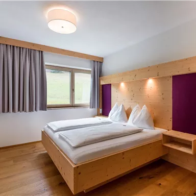 Ein gemütliches Schlafzimmer mit einem großen Bett und Holzdecor. Das Zimmer hat ein Fenster mit Blick auf die Natur und sanfte Beleuchtung.
