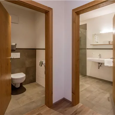 Zwei Badezimmer mit modernen Einrichtungen. Die linke Seite hat eine Toilette und die rechte Seite eine Dusche mit Waschbecken.