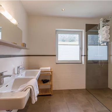 Ein modernes Badezimmer mit zwei Waschbecken und einer Dusche. Helle Farben und natürliche Lichtquellen schaffen eine einladende Atmosphäre.