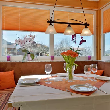 Ein einladender Essbereich mit einem Tisch, der für ein besonderes Abendessen gedeckt ist. Große Fenster bieten einen schönen Ausblick und lassen viel Licht herein.