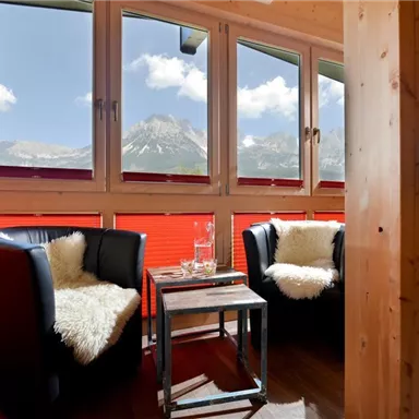 A cozy room with two black armchairs and a small table. Through large windows, there is a view of the mountains and the blue sky.
