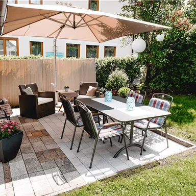 Ein einladender Gartentisch mit Stühlen unter einem Sonnenschirm. Umgeben von grünen Pflanzen und einer gemütlichen Sitzecke.