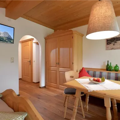 Ein gemütlicher Wohnbereich mit Holzmöbeln und einem Esstisch. An den Wänden hängen Bilder von Landschaften und die Dekoration sorgt für eine einladende Atmosphäre.