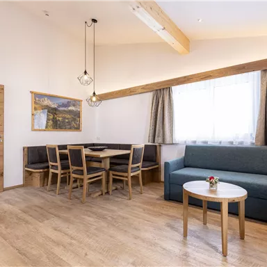 Ein modernes Wohnzimmer mit einem bequemen Sofa und einem Esstisch. Große Fenster sorgen für viel Tageslicht und eine gemütliche Atmosphäre.