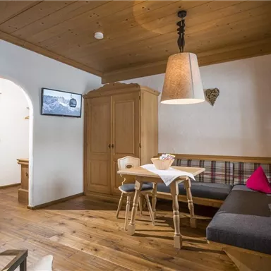 Ein gemütlicher Wohnraum mit Holzverkleidung und einem großen Tisch. Der Raum ist hell und verfügt über eine Leseecke sowie eine moderne Küche.