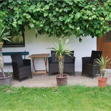 A cozy seating area with two chairs and a table, surrounded by plants. In the background, a wooden door can be seen.