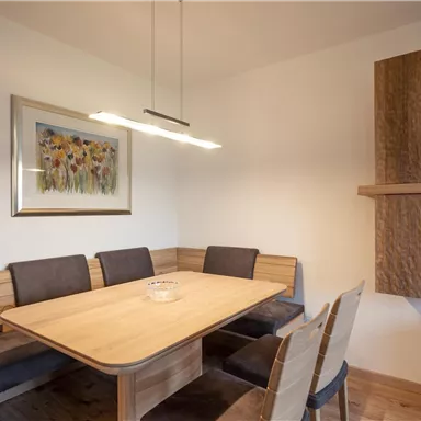 A modern dining area with a wooden table and comfortable benches. A painting with colorful flowers hangs on the wall.