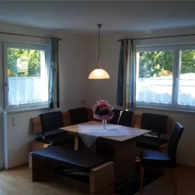Ein gemütlicher Essbereich mit einem runden Tisch und einer Bank. Große Fenster lassen viel Licht herein und bieten einen Blick in den Garten.