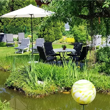 A beautiful garden with a pond and cozy seating areas. The scene is surrounded by green plants and offers a relaxing atmosphere.