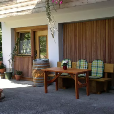 Ein behaglicher Eingangsbereich mit einem Holztisch und Stühlen. Verschiedene Pflanzen in Töpfen und ein großes Fass schaffen eine einladende Atmosphäre.