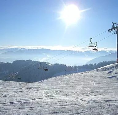 A beautiful winter landscape with snow-covered mountains. Ski lifts are in the foreground, and the sun is shining in the clear sky.