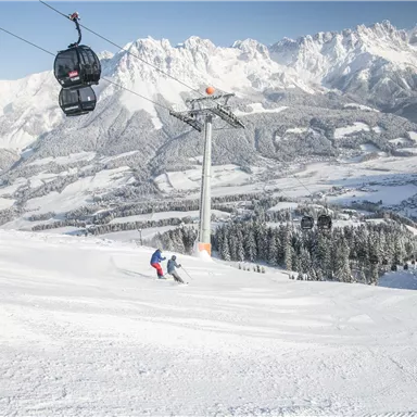 Eine winterliche Berglandschaft mit schneebedeckten Pisten und einer Seilbahn. Skifahrer genießen die wunderbare Aussicht auf die hügelige Umgebung.