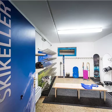 A ski cellar with shelves for sports equipment and a table in the middle. Skis, snowboards, and boots are hanging on the wall.